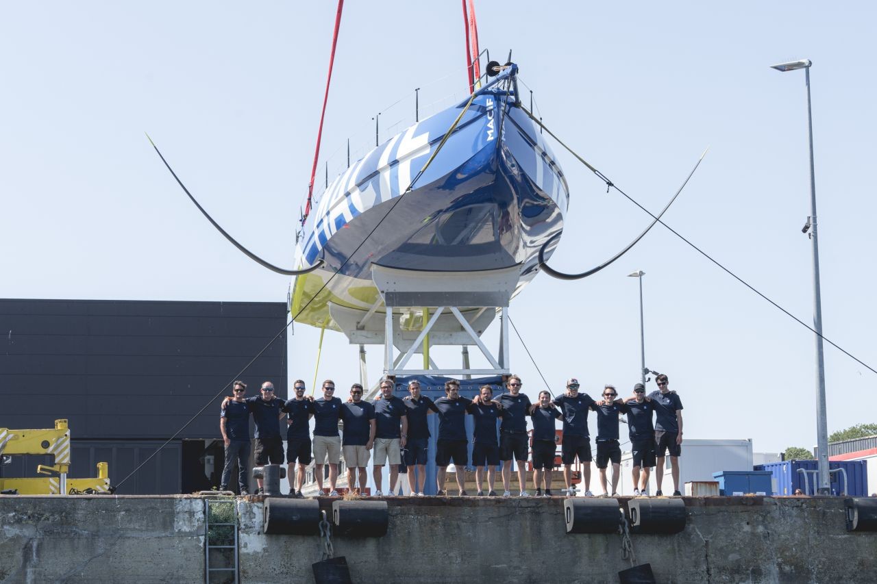 L'IMOCA MACIF suspendu au-dessus de l'équipe alignée sur le quai.