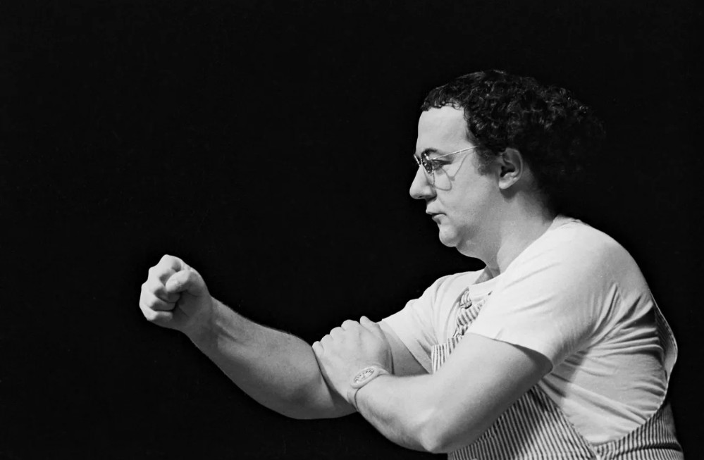 Coluche sur scène, le poing levé, mars 1981