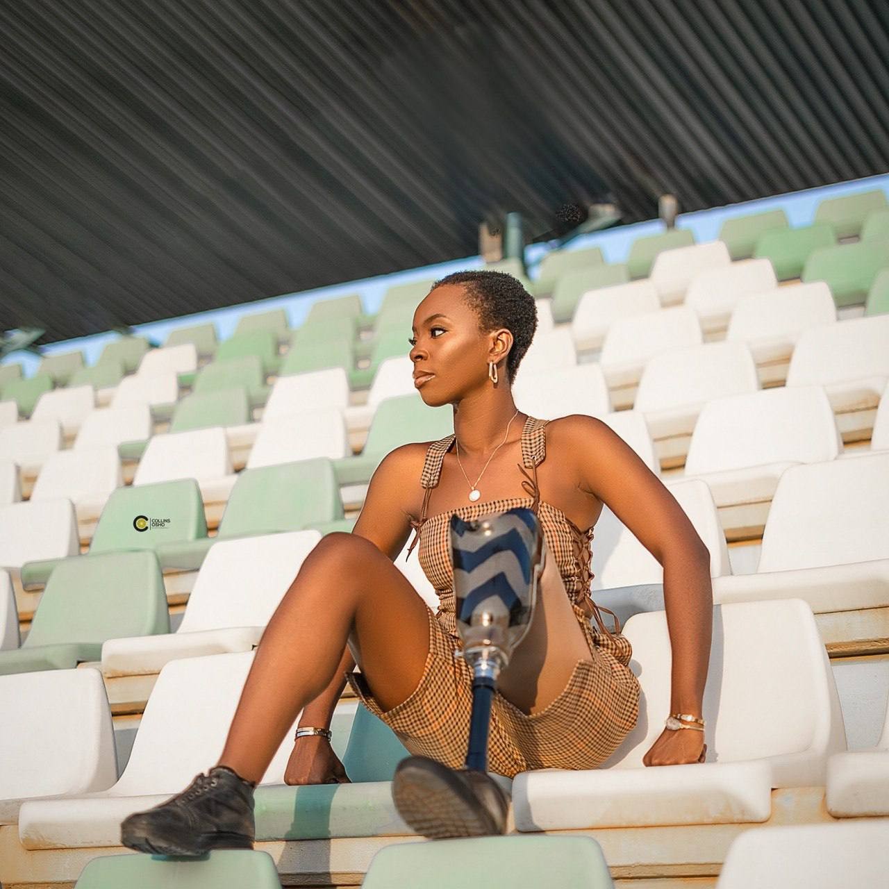 Eva Chisom Chukwunelo sitting alone in stadium stands, her leg prosthesis visible