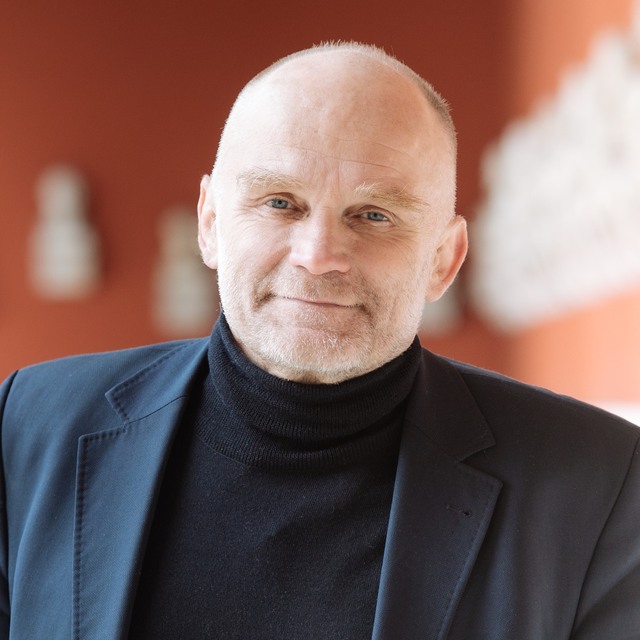 Portrait of Frédéric Petit, black jacket and turtleneck against a red background