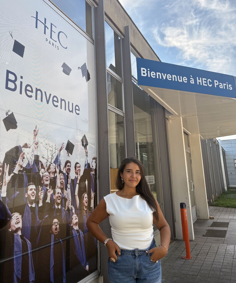 Inès Ahaggan devant l’entrée de HEC Paris, sous l’enseigne « Bienvenue à HEC Paris »