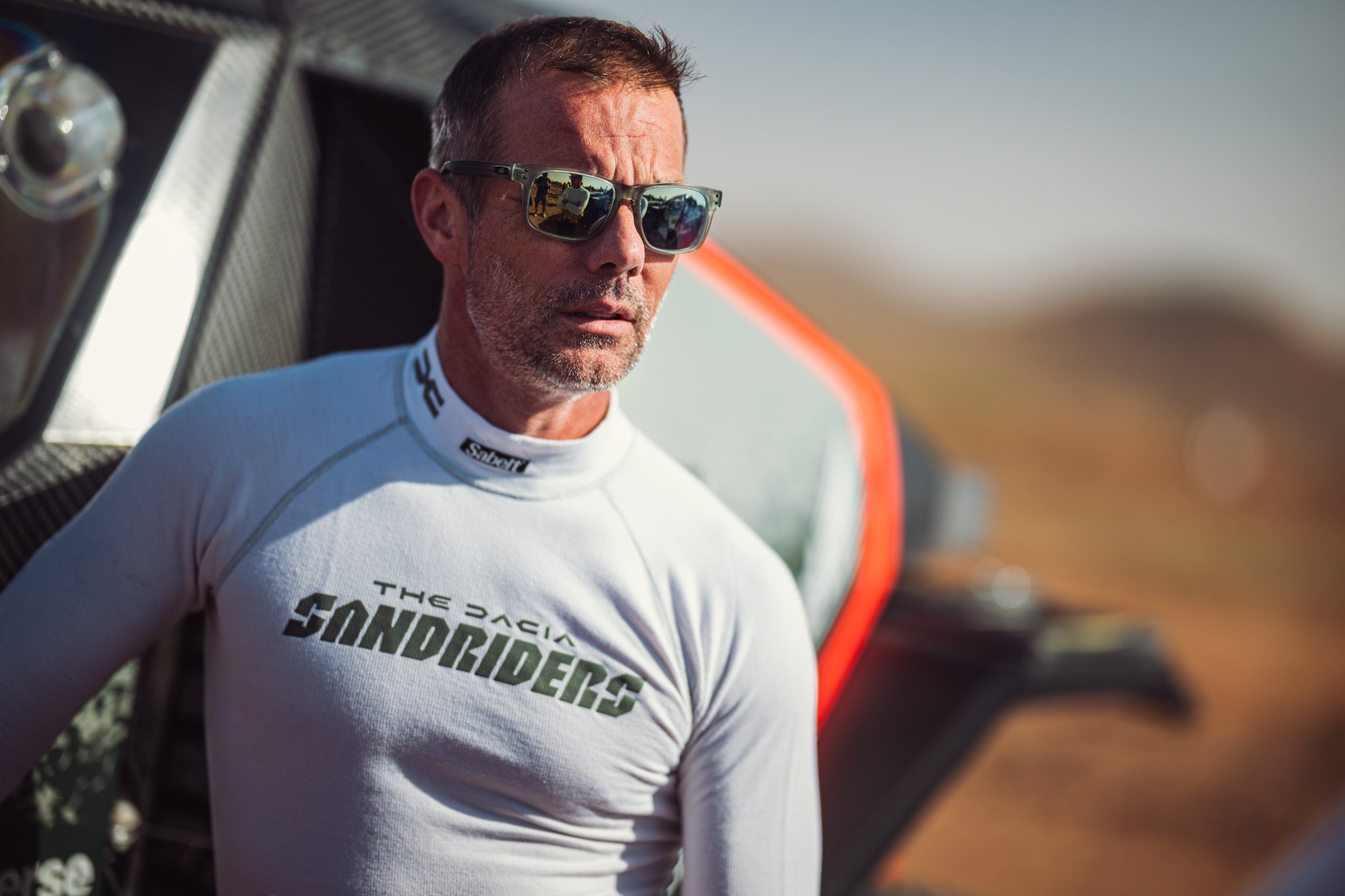 Sébastien Loeb wearing sunglasses beside his Dacia Sandriders car